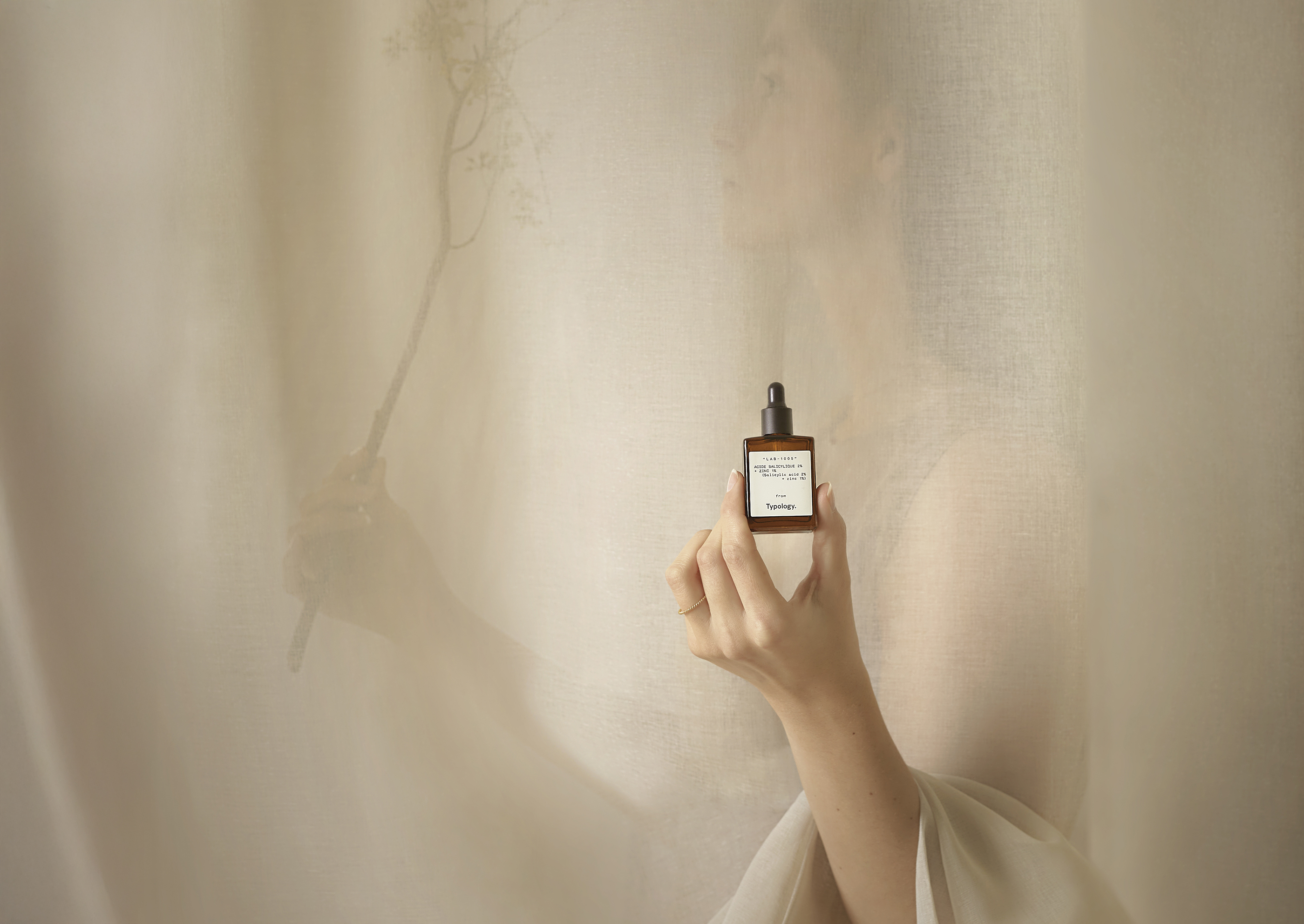 Typology Product Photography showing a female silhouette through a curtain holding a skin care product
